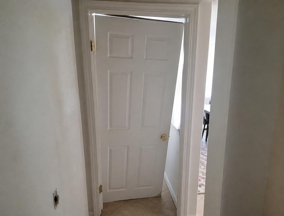 Sagging interior door hanging crooked in its frame with a broken hinge