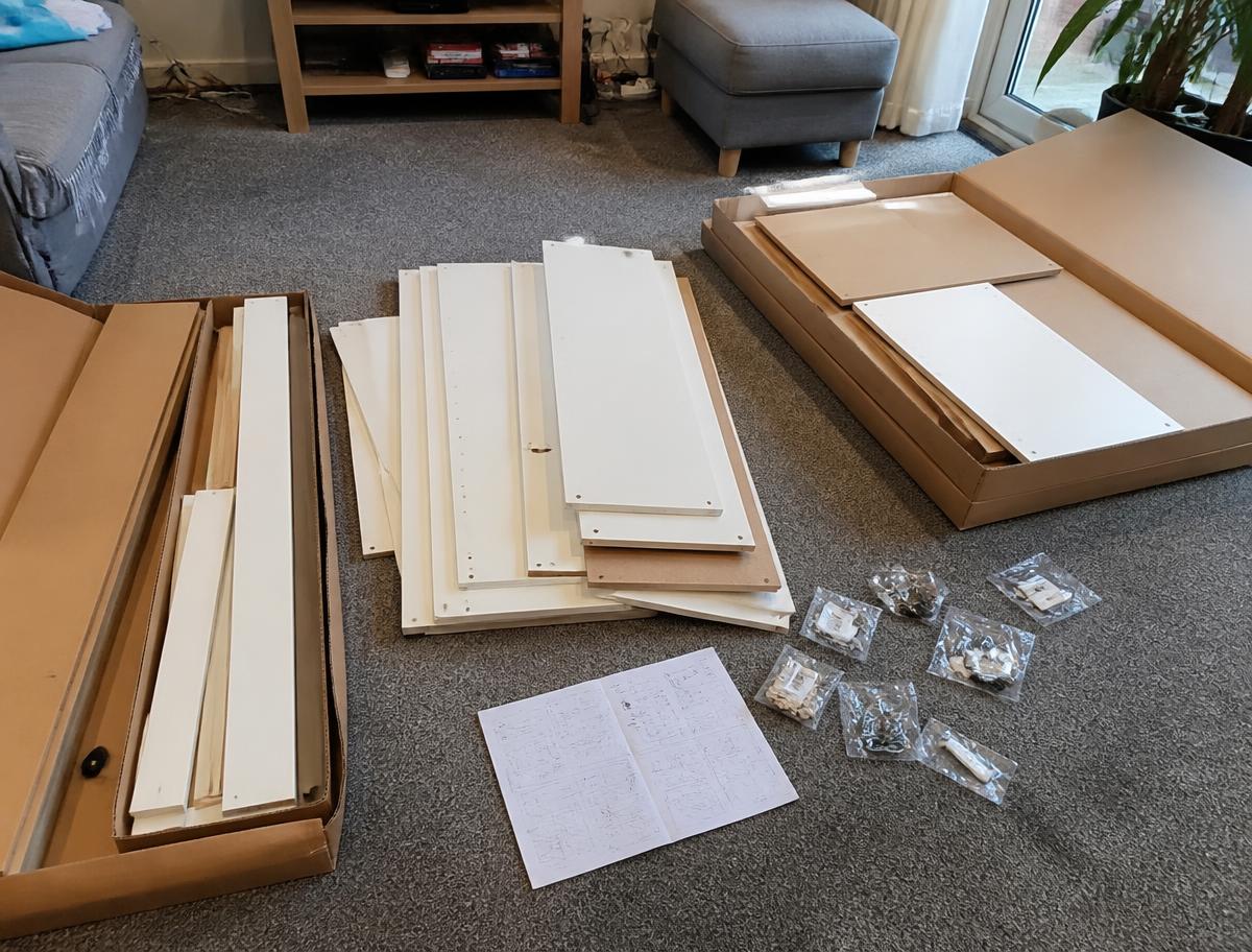 Flat pack furniture panels and hardware bags spread out on a living room floor