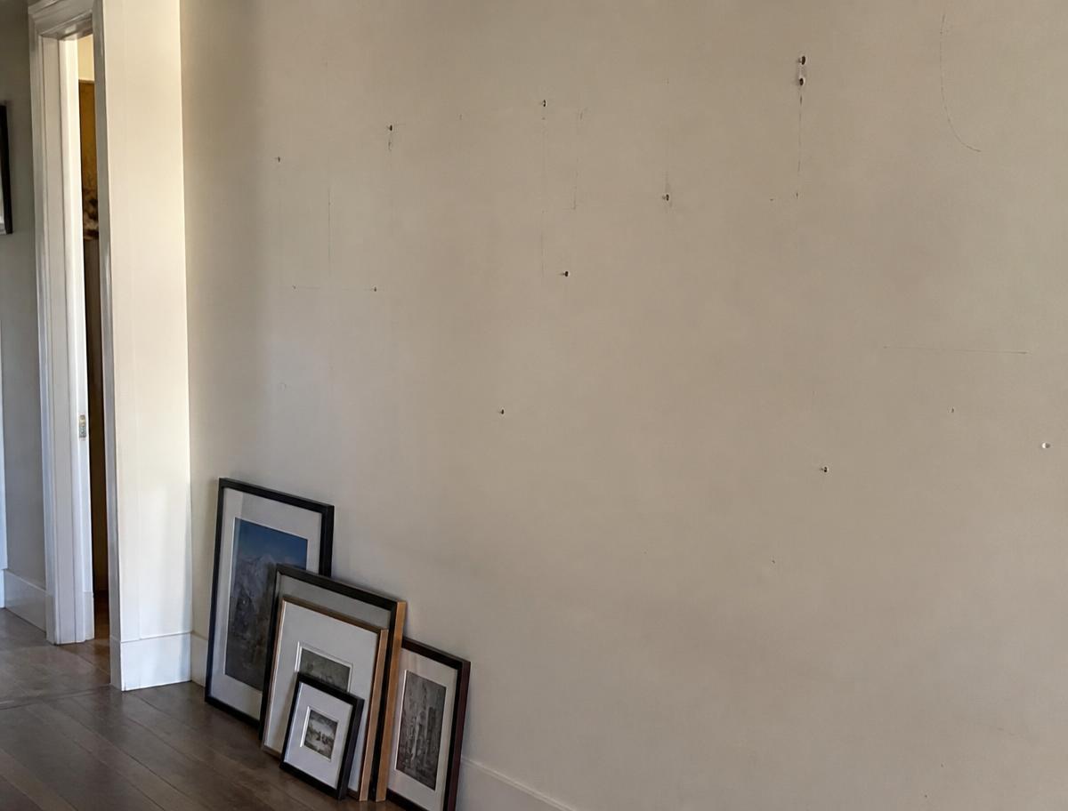Bare hallway wall with old nail holes and framed pictures leaning against the baseboard