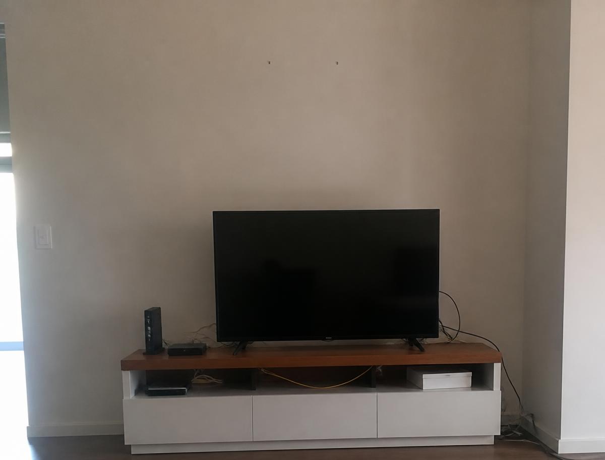 TV sitting on a console with messy dangling cables and a bare wall above